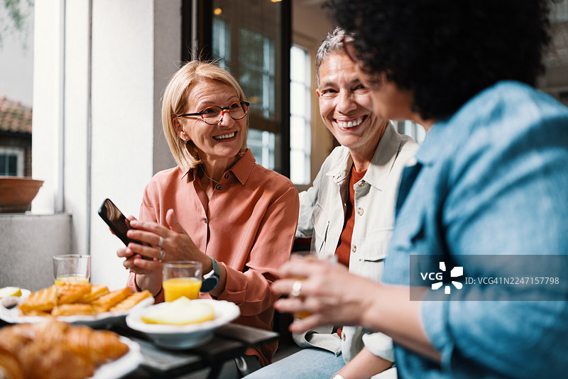 三位中年女性在吃早午餐时，边看约会软件边大笑图片素材