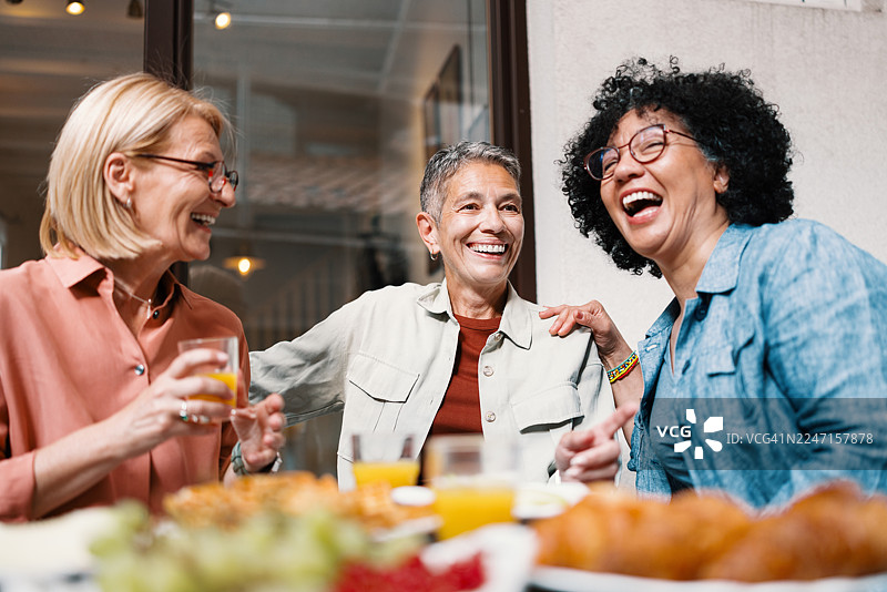 三位中年女性在吃早午餐时，一边浏览约会应用程序一边大笑图片素材