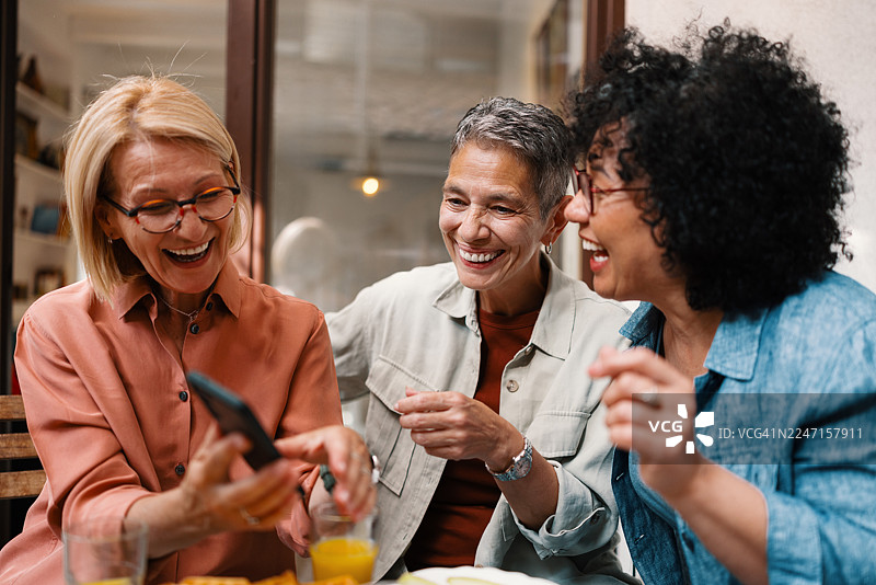 成熟的朋友们在户外早午餐时，一边使用手机一边分享有趣的时刻图片素材