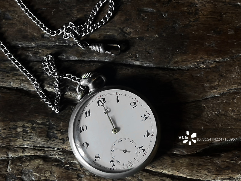 银质的古董怀表及其表链，放置在木质表面上。图片素材