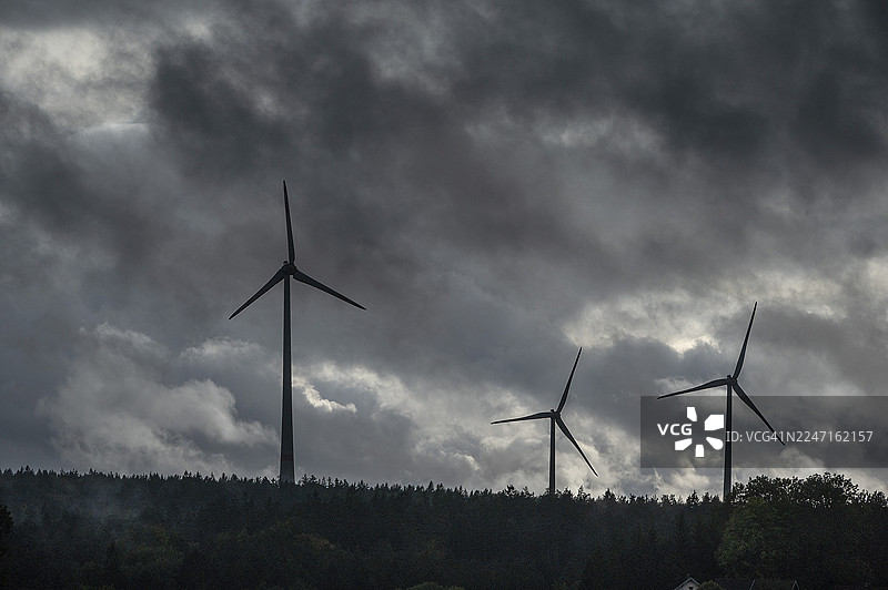 风力涡轮机在雷雨天气下位于松树林中，巴伐利亚森林，巴伐利亚，德国图片素材