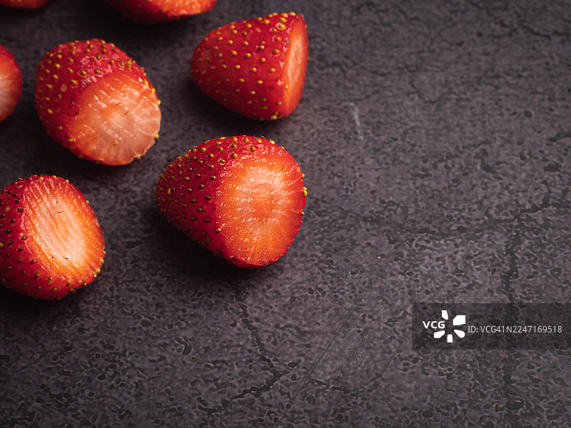 俯视视角，深色纹理表面上放着切半的新鲜成熟草莓，留有复制空间图片素材