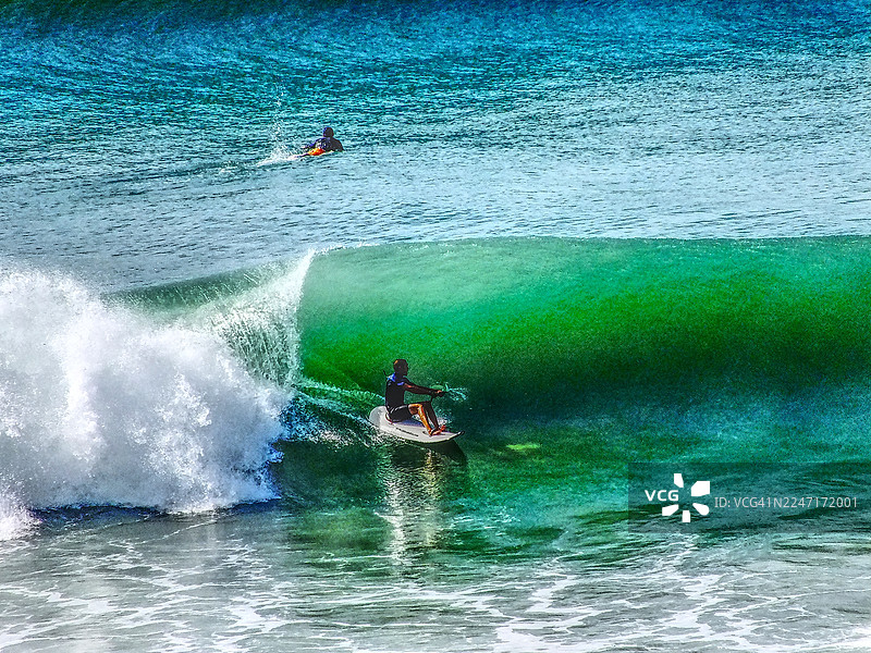 俯视视角，一名男子在冲浪板上乘浪，背景中另有一人，享受着海洋运动图片素材