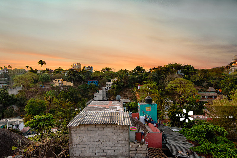墨西哥萨尤利塔，俯瞰色彩斑斓的日落天空下，郁郁葱葱的树木环绕的充满活力的山坡小镇图片素材