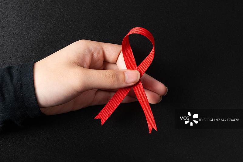 特写一只手拿着红色丝带，背景为深色，象征着对健康事业的支持图片素材