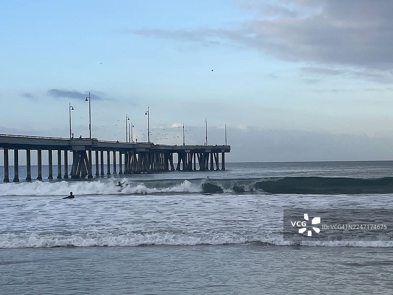美国洛杉矶威尼斯海滩，多云天气下，海上木板栈道上的风景，海浪中有冲浪者图片素材