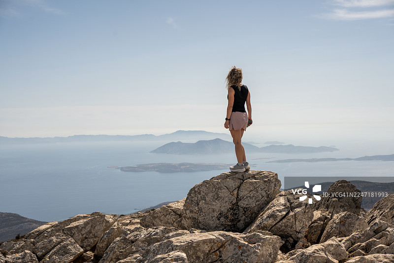 年轻女子站在扎斯山的顶峰，这里是基克拉泽斯群岛（希腊纳克索斯岛）的最高点。图片素材