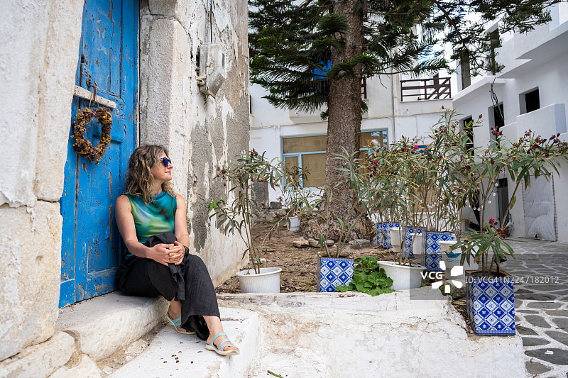 一位女子坐在希腊纳克索斯老城一扇古老门前的地面上图片素材