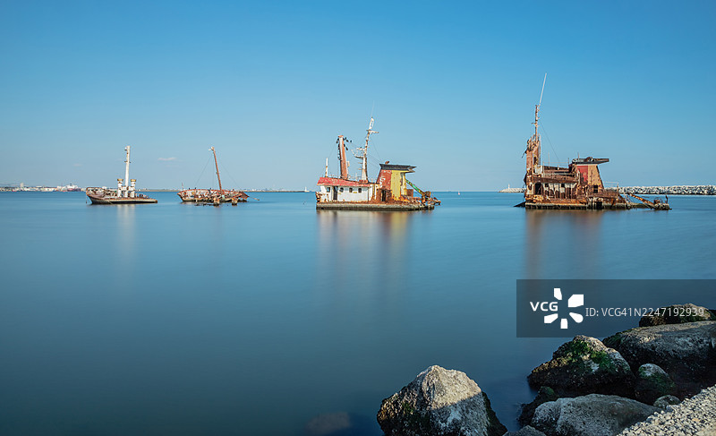 晴朗天空下，平静蓝色大海中废弃生锈的沉船的长时间曝光景象图片素材