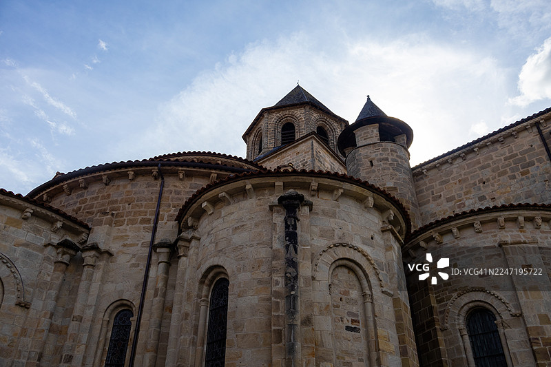 从低角度仰视一座古老的石头教堂，背景是明亮的天空，展示了精美的建筑细节和历史韵味，法国，康塔尔图片素材