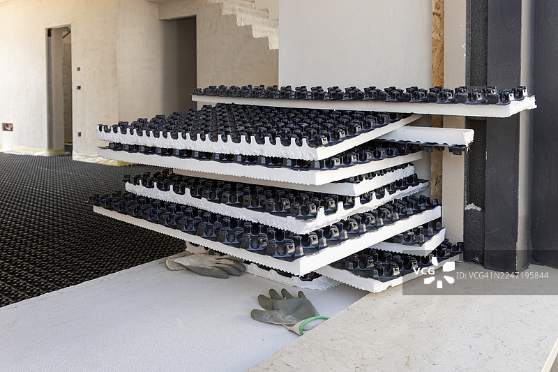 建筑工地上，地板上铺设着堆叠的保温板和手套，展示了地板供暖系统的安装过程图片素材