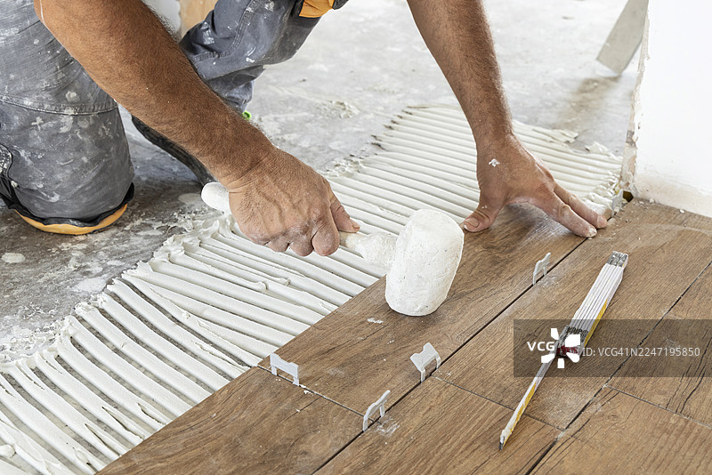 施工现场的工人正在使用粘合剂和橡胶锤安装陶瓷地板砖图片素材