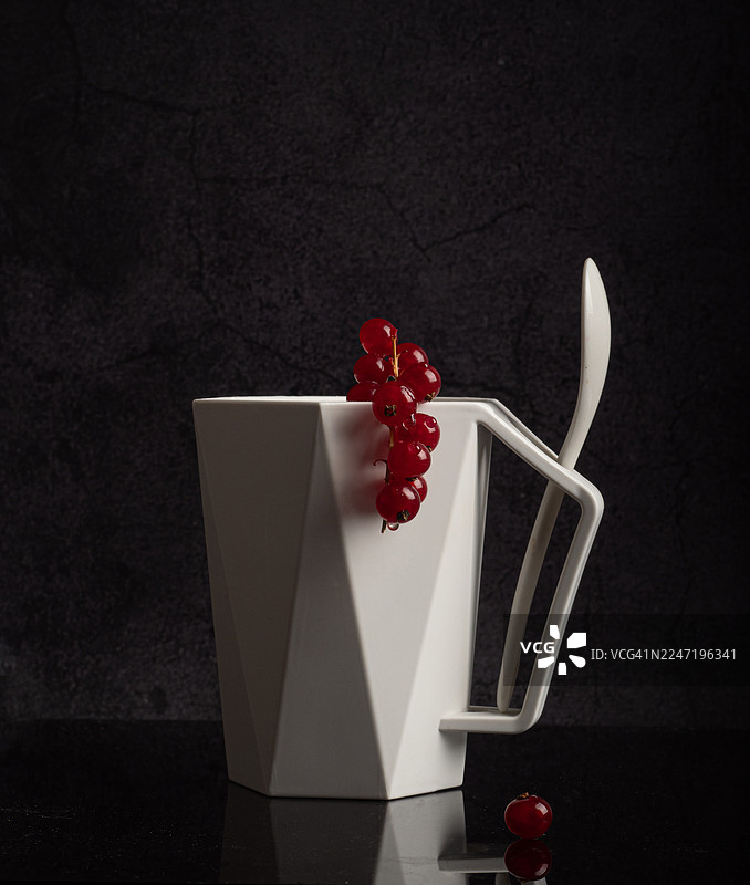 深色背景上带有红醋栗和勺子的白色几何马克杯图片素材