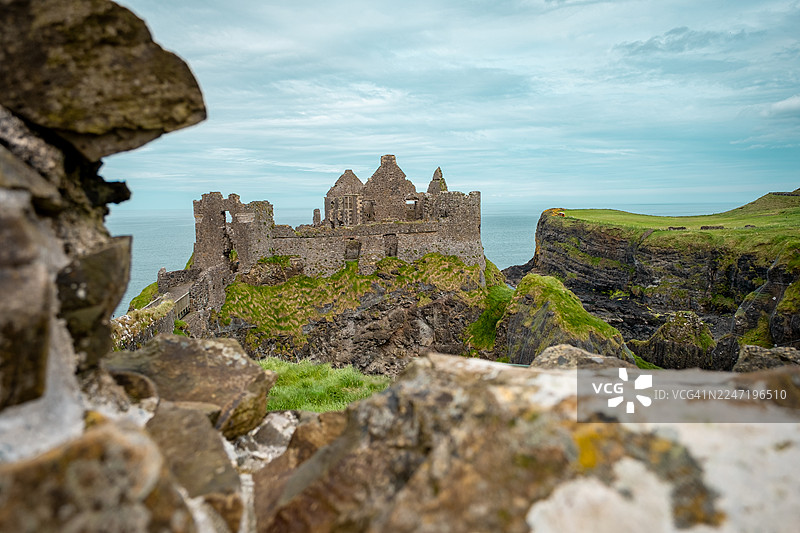英国邓路斯城堡，阴云密布的天空下，坐落在悬崖上俯瞰大海的古老城堡遗址的戏剧性景观图片素材