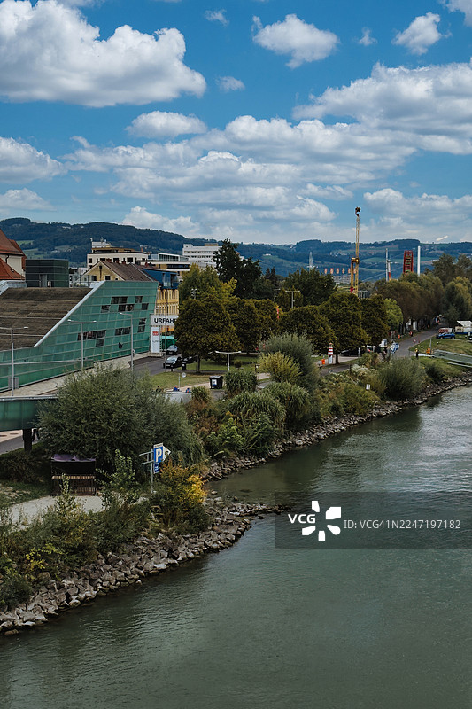 奥地利林茨，城市建筑和茂密绿树旁的风景优美的河流，蓝天白云图片素材