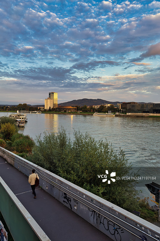 奥地利林茨，夕阳下，戏剧般的天空映衬着城市建筑和远处的山峦，风景如画的河流景色图片素材