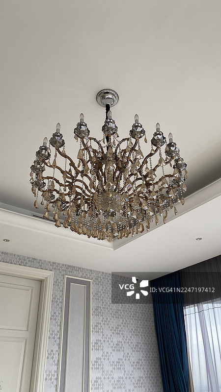优雅的水晶吊灯悬挂在白色天花板上，房间里有图案壁纸和蓝色窗帘，印度尼西亚图片素材