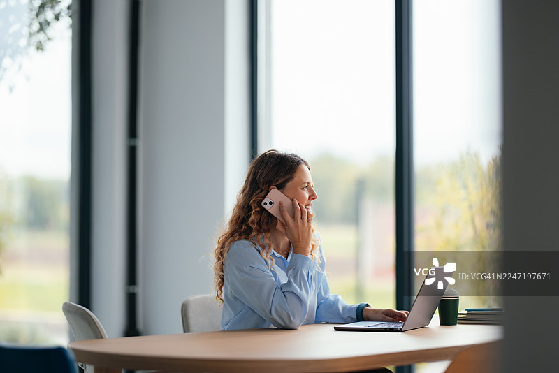 职业女性在工作日于办公室使用笔记本电脑接听电话，旁边放着咖啡杯图片素材
