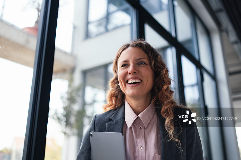 一位快乐的女商人在办公室使用平板电脑，在会议或谈话中面带微笑图片素材