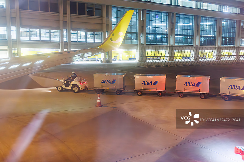 我们抵达了那霸机场。行李车、牵引车和其他车辆正在工作。机场工作人员正在装载行李。图片素材