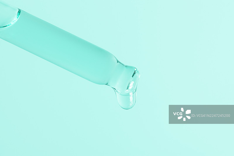 滴管滴下的液滴置于薄荷绿背景上，展现实验室的精准、化学和科学的瞬间图片素材