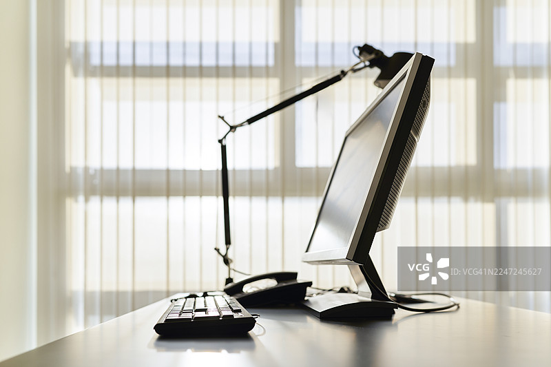 窗户旁的办公桌，配有电脑和键盘图片素材