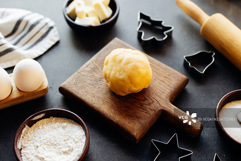 面团在木板上，周围是烘焙原料，包括鸡蛋、黄油、面粉和饼干模具，营造出节日烘焙的喜庆气氛图片素材