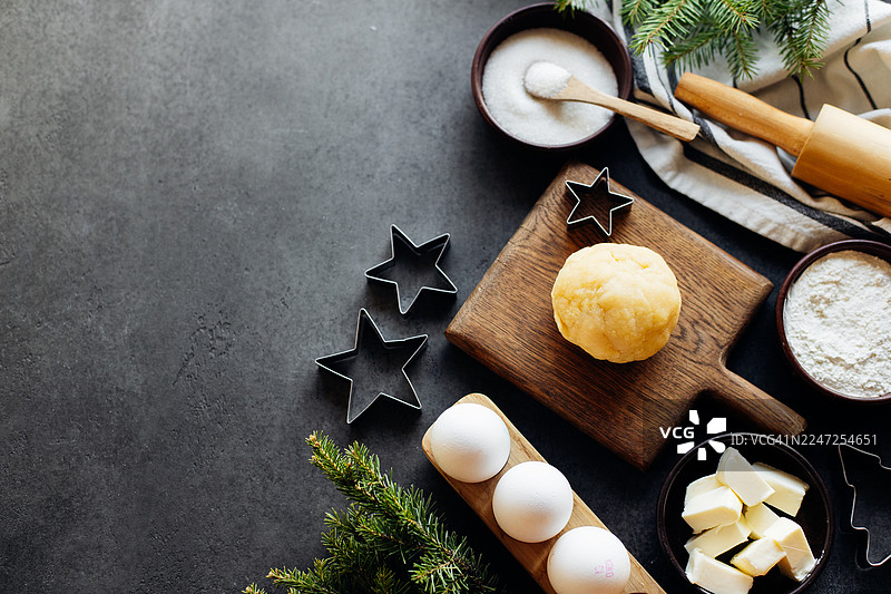 面团在木板上，周围摆放着烘焙原料，包括鸡蛋、面粉、黄油和饼干模具，营造出节日烘焙的喜庆氛围图片素材