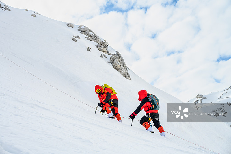 身着鲜艳装备的登山者，坚定地攀登着白雪皑皑的高山斜坡图片素材