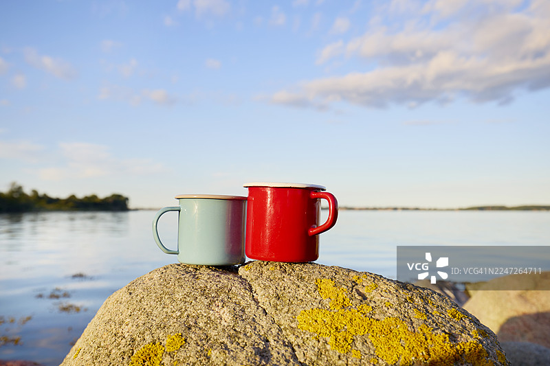 海边岩石上的红蓝珐琅咖啡杯图片素材