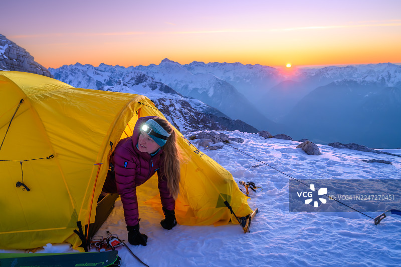 日出时，一位中年高加索女性正在雪山中走出帐篷图片素材