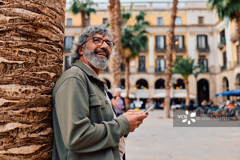 一位年长的男士在巴塞罗那城市广场上微笑着使用手机图片素材