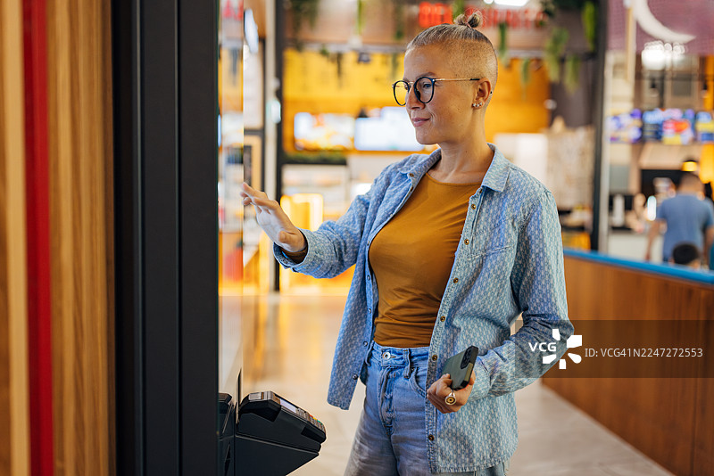 一位女性顾客在现代快餐店使用数字自助点餐机。该女子正通过触摸屏技术定制她的餐点选择。图片素材