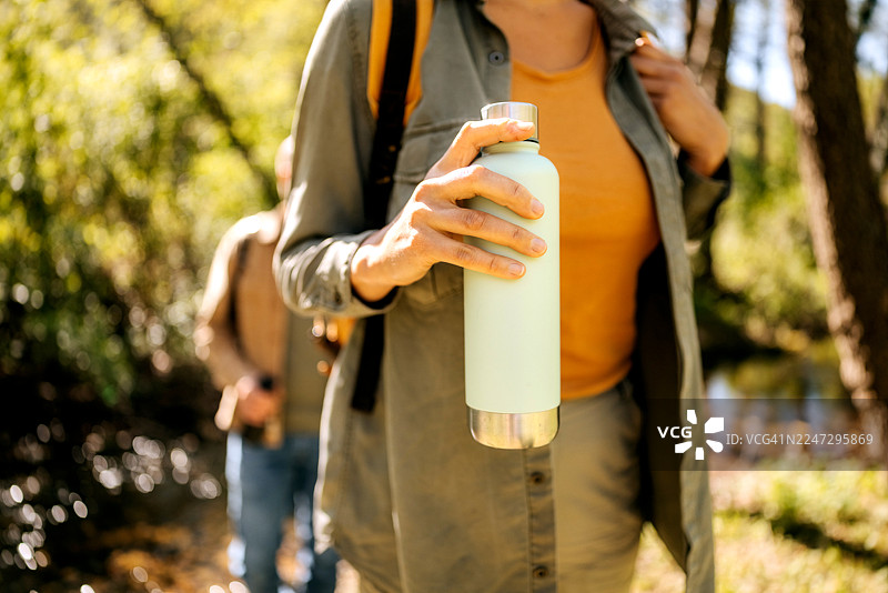阳光明媚的日子里，一位女士在山中手持保温瓶饮水图片素材