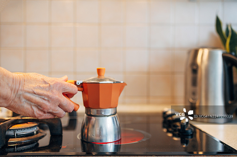 老人的手将摩卡壶放在厨房炉灶上图片素材