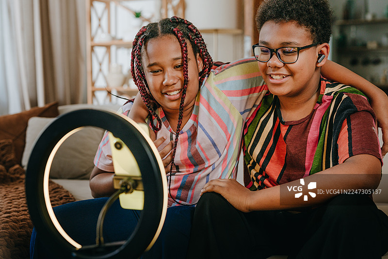 兄妹俩在家用智能手机和环形灯录制视频内容图片素材