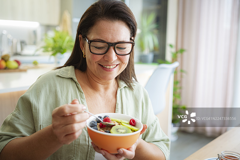 一位女士在家吃谷物和水果的肖像。她正享用健康的餐食，这是早晨的一餐，也可以是午餐、早餐或任何一餐。图片素材