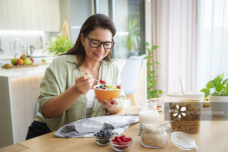 一位成熟的女性在家中吃谷物和水果。健康饮食和节食概念。早餐或正餐。早晨坐在桌边。图片素材