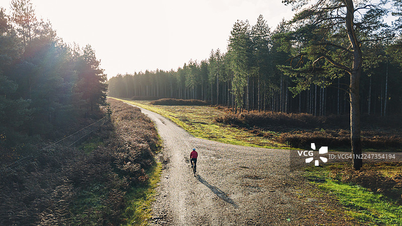 无人机/高空视角：秋日晴朗的早晨，一位成熟的男士正骑着他的砾石自行车探索森林。图片素材