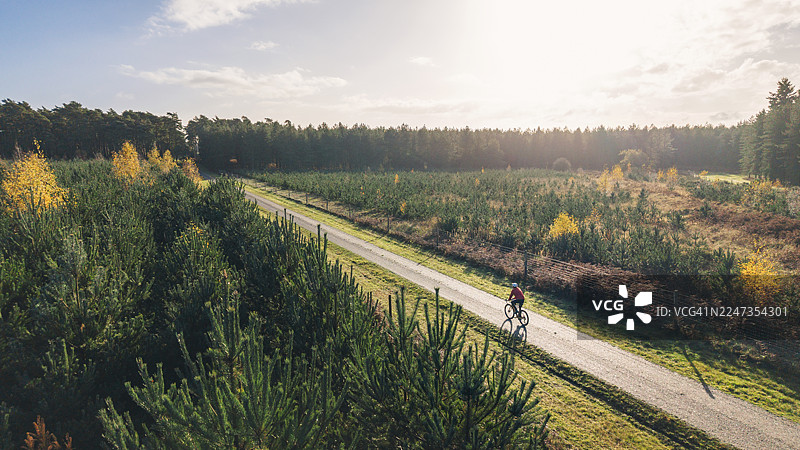 无人机/高视角拍摄：一位成熟的男士在阳光明媚的秋日早晨，骑着砂石公路车探索森林图片素材