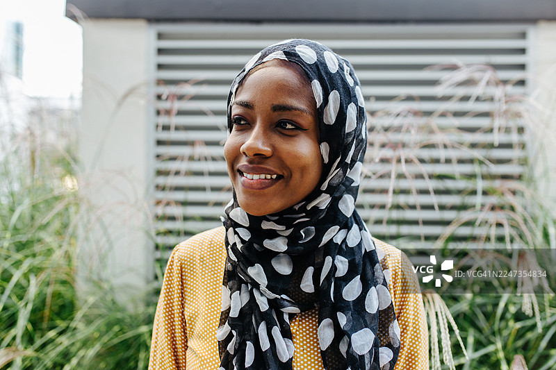 戴着头巾的穆斯林女性在户外微笑，看向别处图片素材
