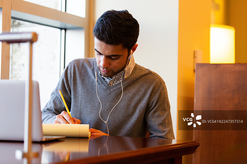 年轻男学生戴着耳机在室内学习，专注于写作图片素材