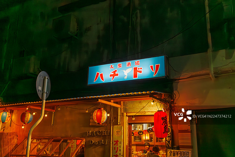 日式居酒屋外观。设有露天吧台，展示着老式踏板车。游客正进入店内，偶尔有出租车经过。图片素材