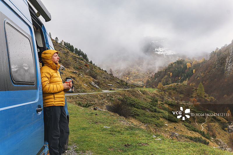 一个成熟的男人在一个下雨的秋日，从他的露营车里眺望着法国比利牛斯山被云雾遮挡的景色图片素材