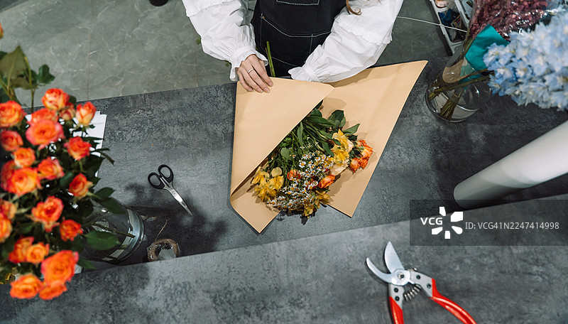 花艺师用牛皮纸包裹混合花束的俯视图图片素材
