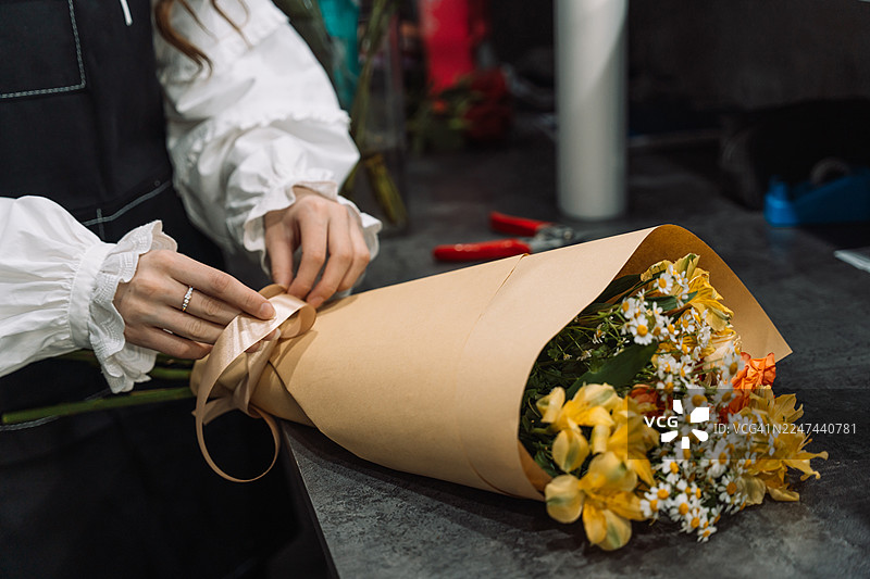 花艺师正在用缎带给牛皮纸包装的花束系上蝴蝶结图片素材