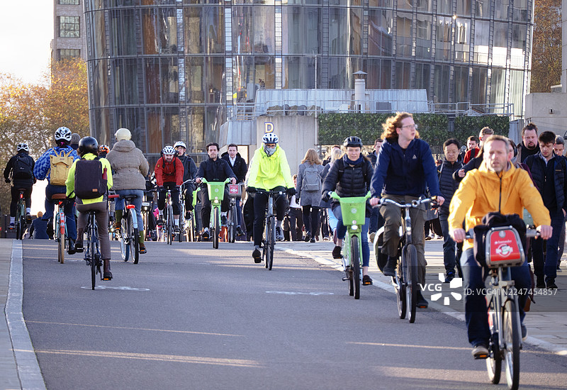 阳光明媚的秋日清晨，通勤者骑车或步行穿越早高峰图片素材