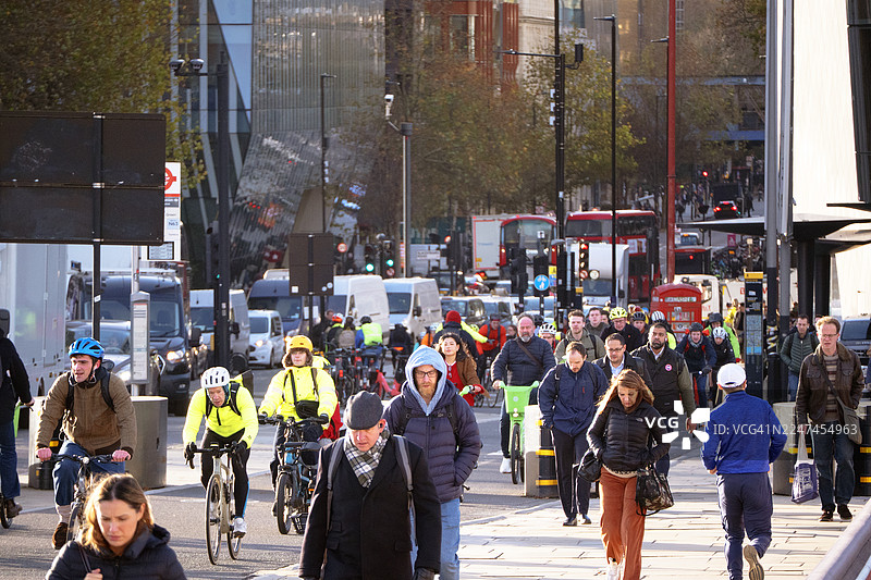 阳光明媚的秋日清晨，通勤者们骑行或步行在早高峰的街道上图片素材