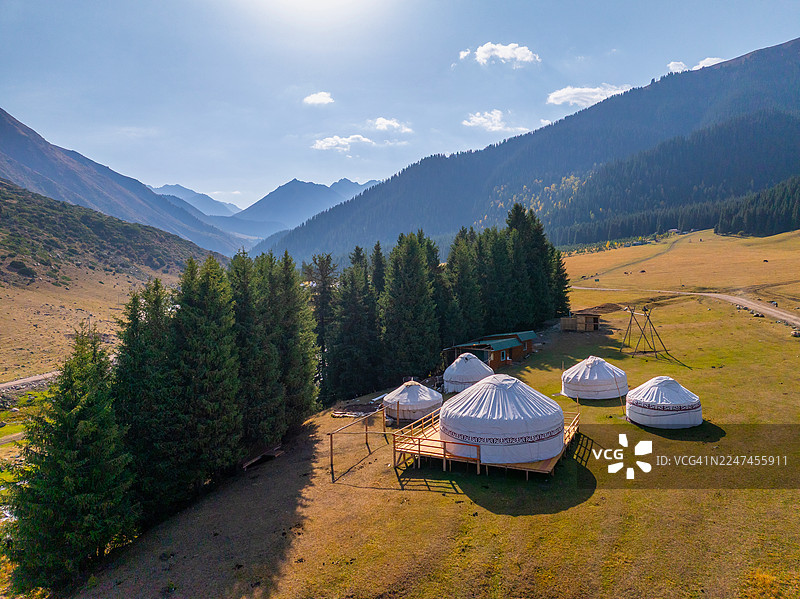 吉尔吉斯斯坦天山山脉中，晨光下的密集针叶林与蜿蜒的冰川河及土路俯瞰视角抽象图。图片素材