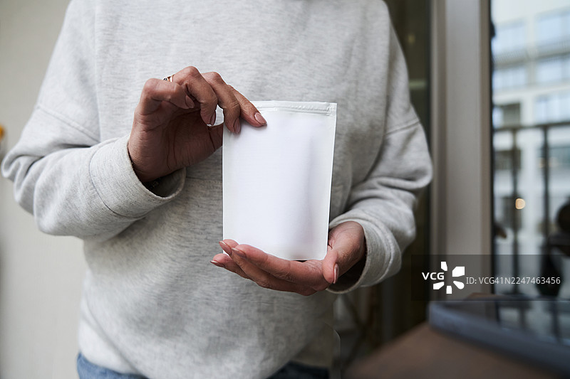 产品模型。一位身穿白色连帽衫的女性手中展示着一袋拉链设计的膳食补充剂。用于产品营销的品牌或标签设计。图片素材